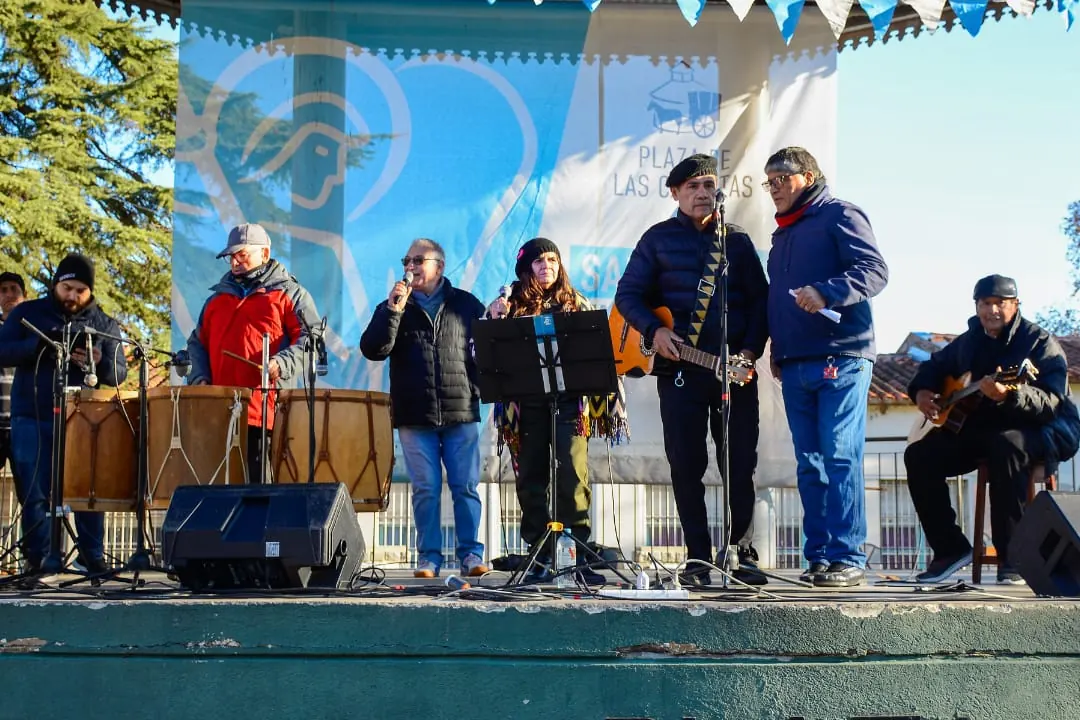Banda de folklore con bombo legüero y percusión en el escenario de una plaza municipal