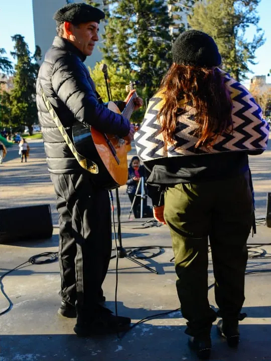 El dúo cantando frente al micrófono en un escenario de plaza en invierno
