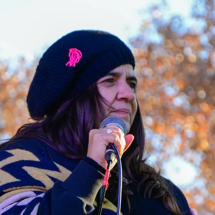 Retrato de Lina cantando al micrófono con poncho y boina negra